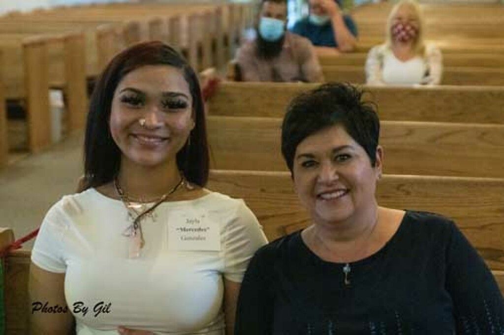 Two people sit closely in a church pew, smiling. 