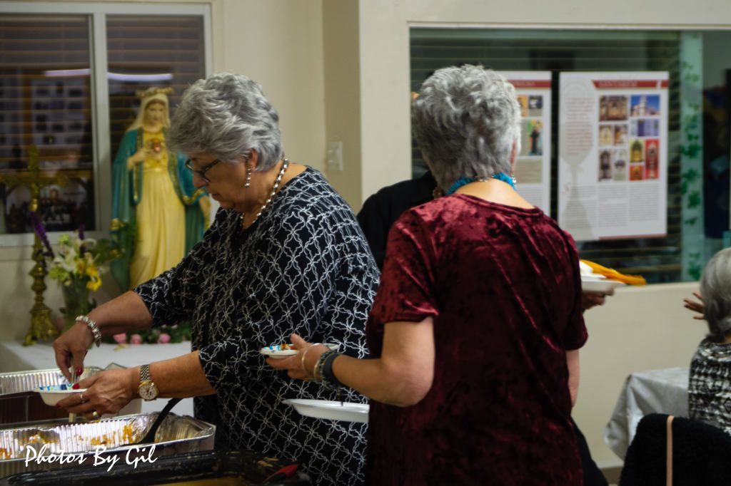 Two older women with gray hair are serving food from buffet trays.