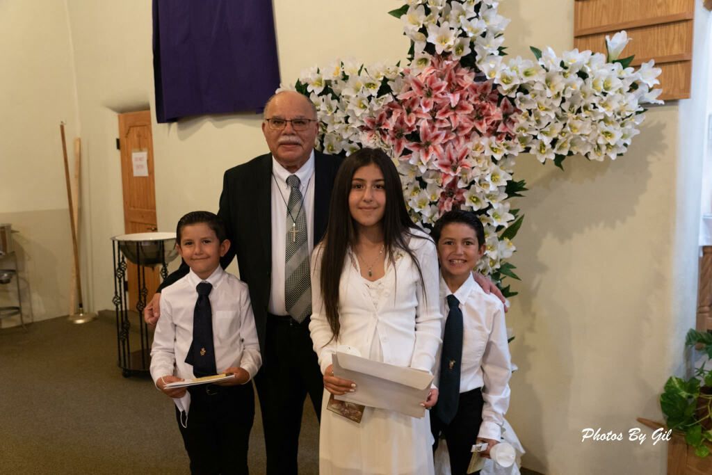 A man in a suit stands with three children in a church, smiling. 