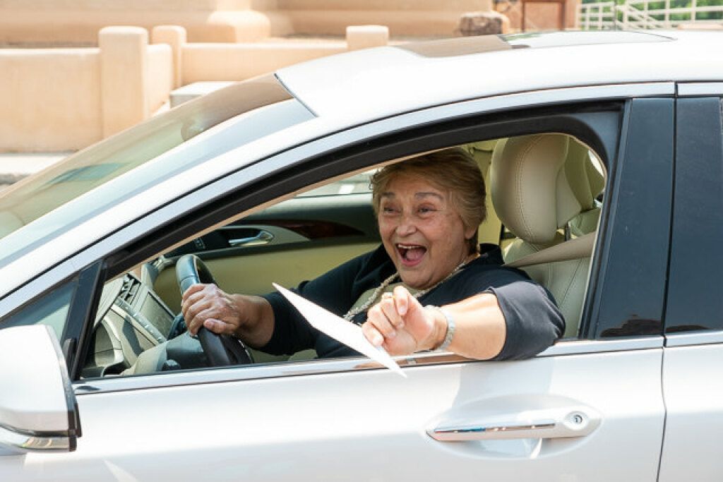 Smiling woman in a white car holding paper, looking out the open window. 