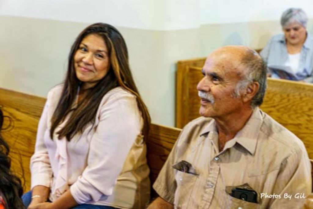 A woman and an older man sit smiling on wooden pews in a church, conveying warmth and contentment. 