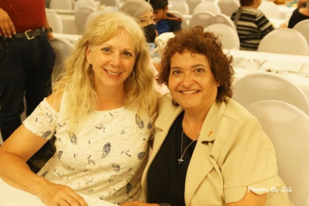 Two women smile warmly at a table in a banquet hall.