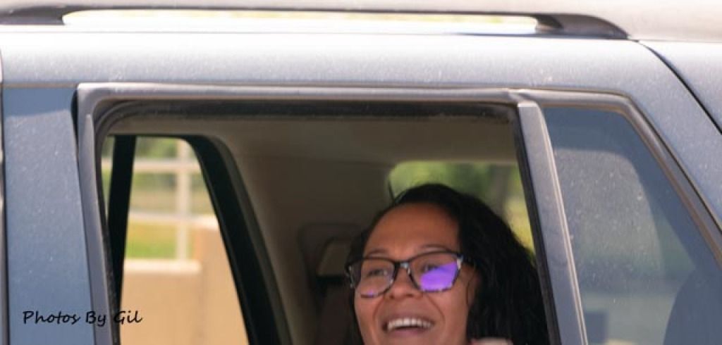 A person with glasses smiling, partially visible through an open car window. 