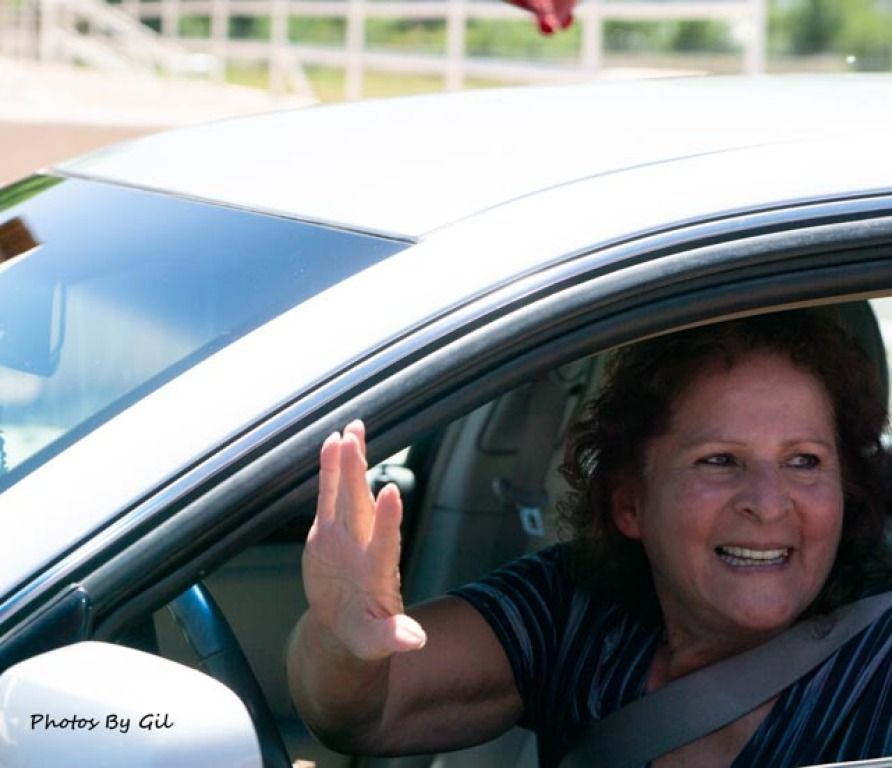 Woman in a car smiles warmly while waving through the open window. 