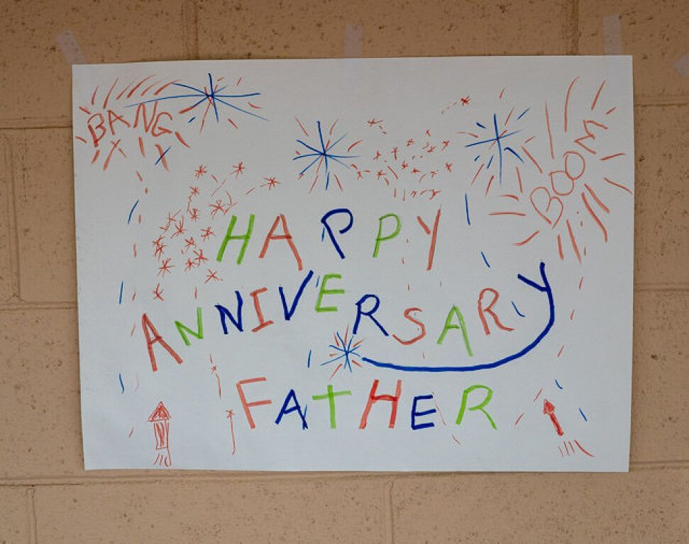 Hand-drawn sign on a wall reads Happy Anniversary Father in colorful letters. 