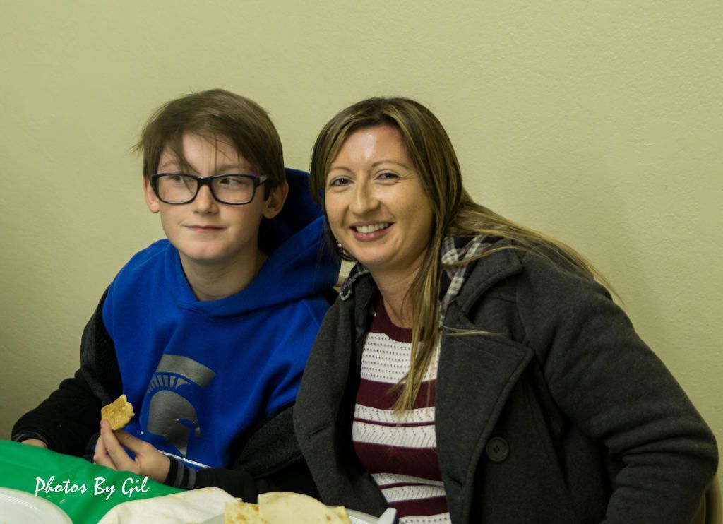 A boy in a blue hoodie sits beside a smiling woman in a gray coat. 