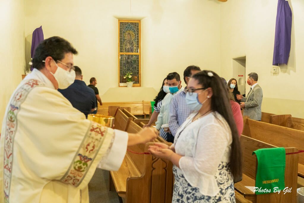 A priest wearing a mask distributes communion to a masked woman in a church. 