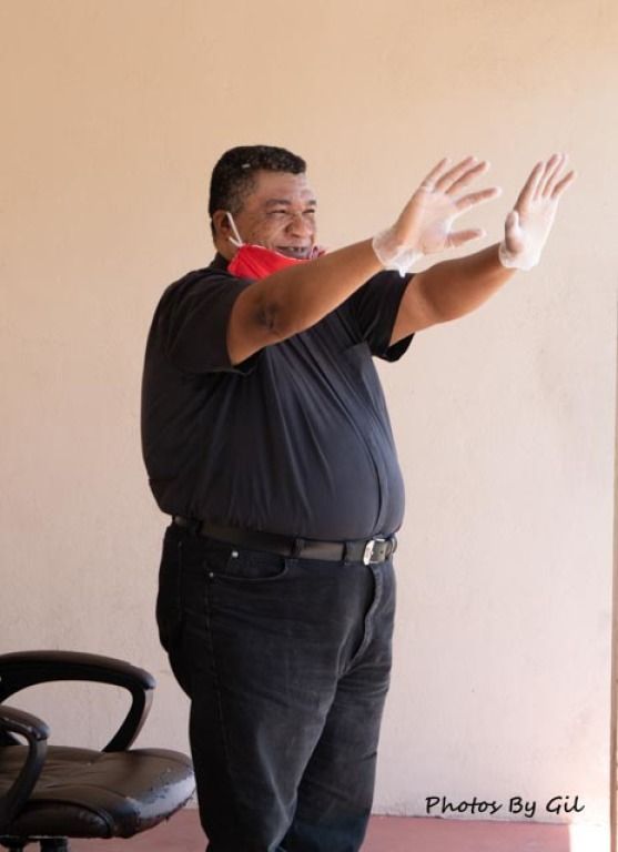 Man in black shirt smiling with outstretched arms, wearing a red face mask and gloves. 