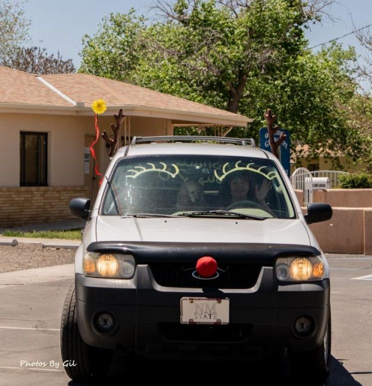 A white SUV decorated like a reindeer with a red nose and antlers on the roof.