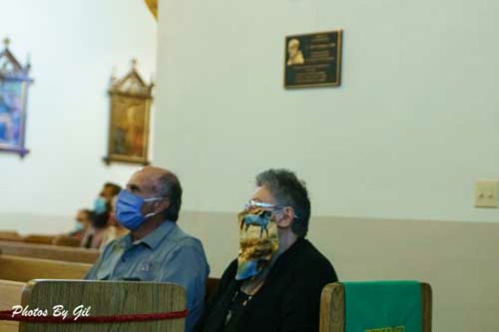 Two people wearing masks sit in a church pew.