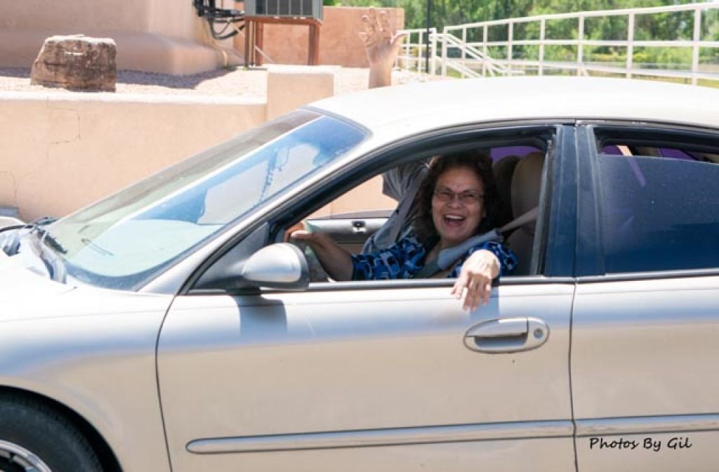 A woman with glasses and a hearty smile is driving a silver car. 