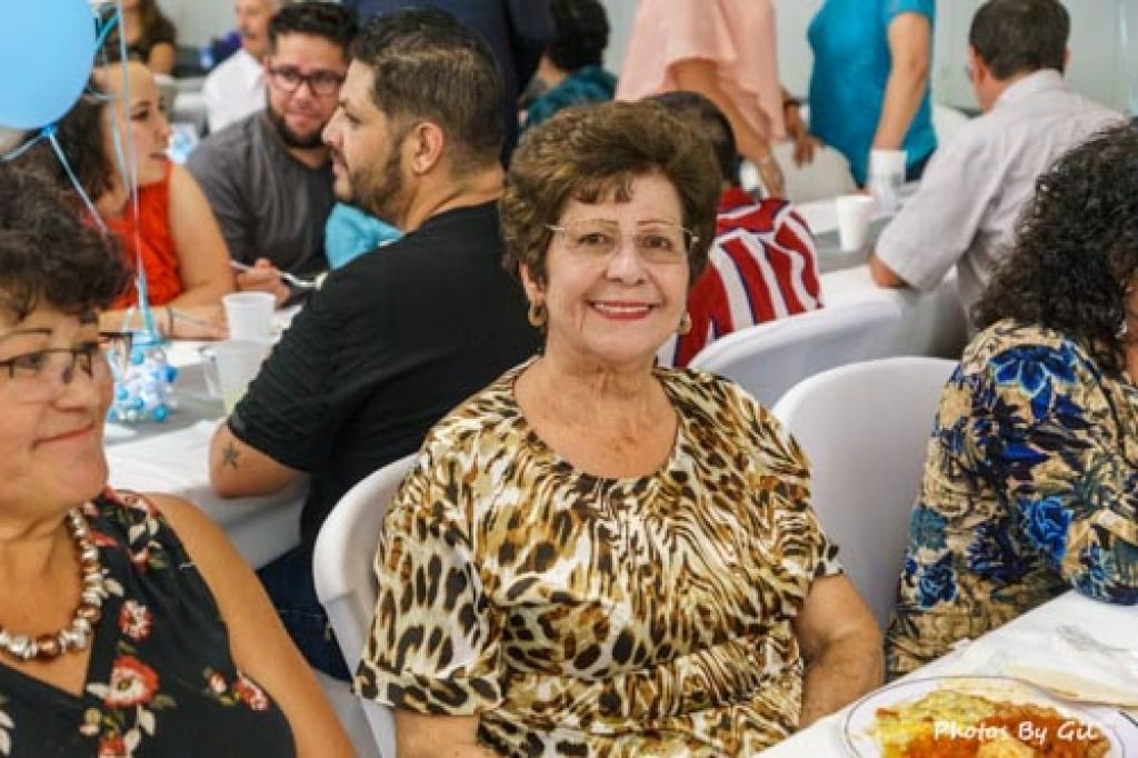 A joyful elderly woman in a leopard print blouse smiles amid a lively gathering.