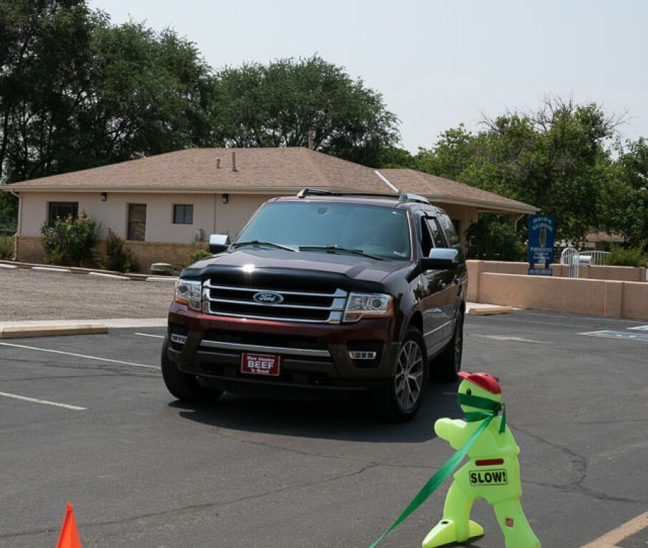 A dark SUV moves through a parking lot near a beige building.