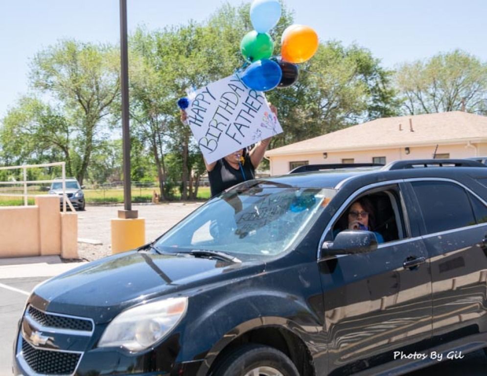A black SUV in a parking lot with a person leaning out of the sunroof, holding colorful balloons.