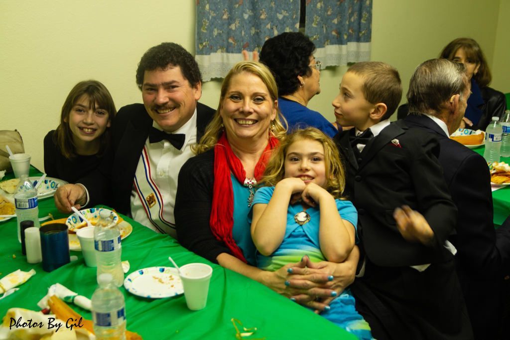 A joyful family gathers around a green table at a celebration. 