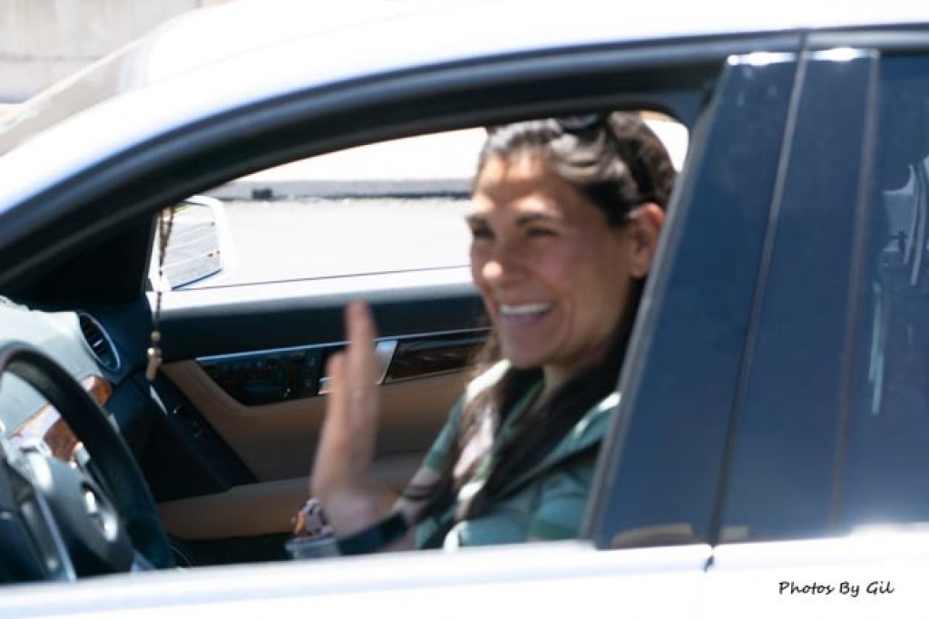 A woman in a car smiles and waves, exuding happiness. 