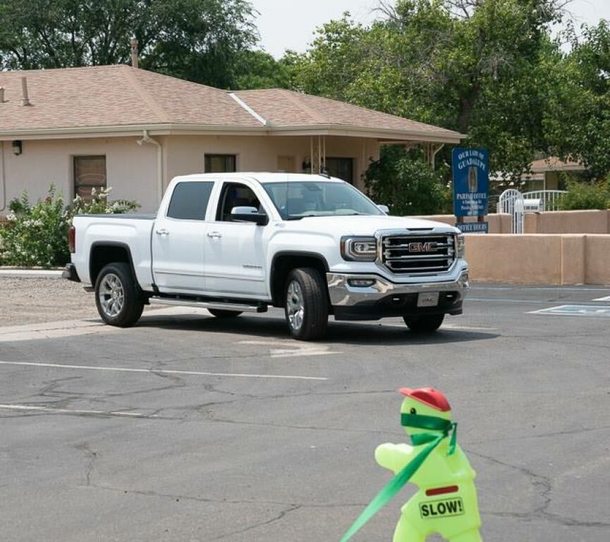 A smiling woman sits in the driver's seat of a parked car, wearing a seatbelt. 