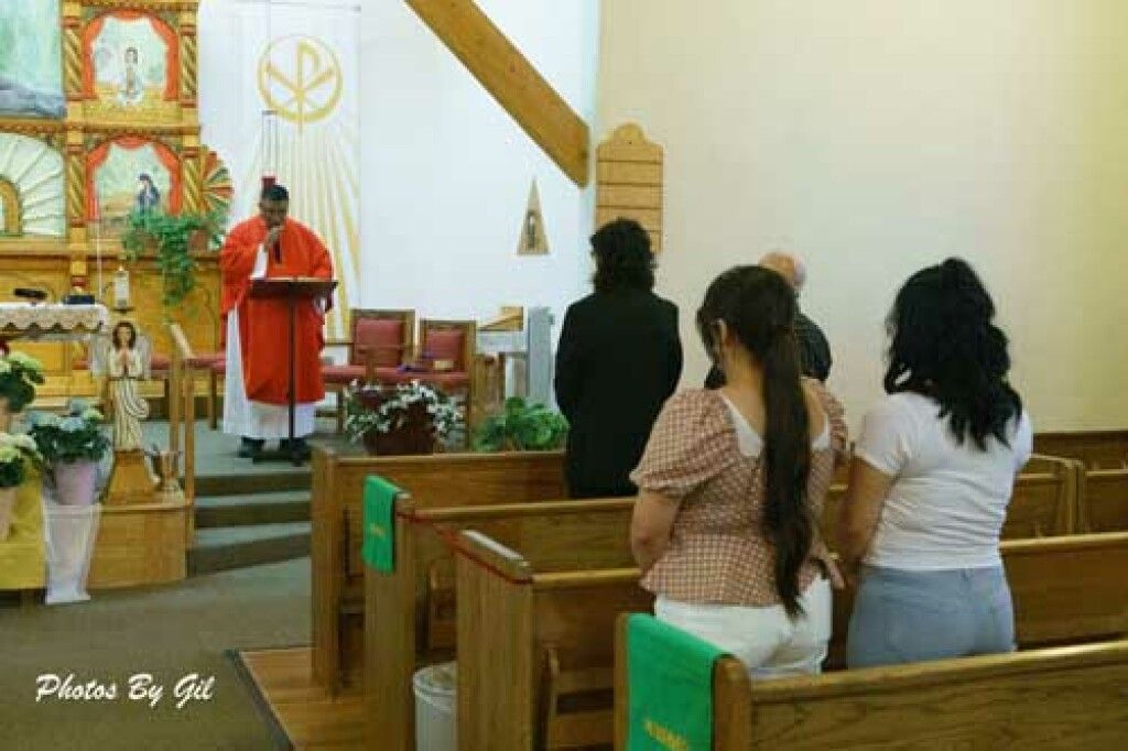 A priest in a red robe stands at the altar reading from a lectern in a church. 
