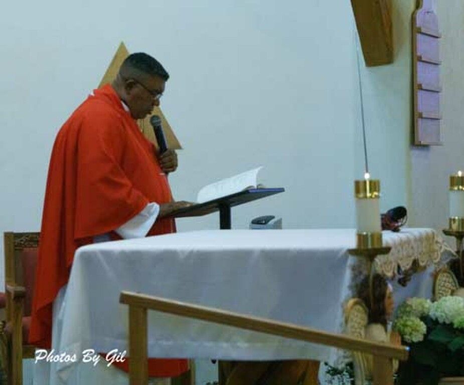 A priest in a red robe reads from a book at a church lectern. 
