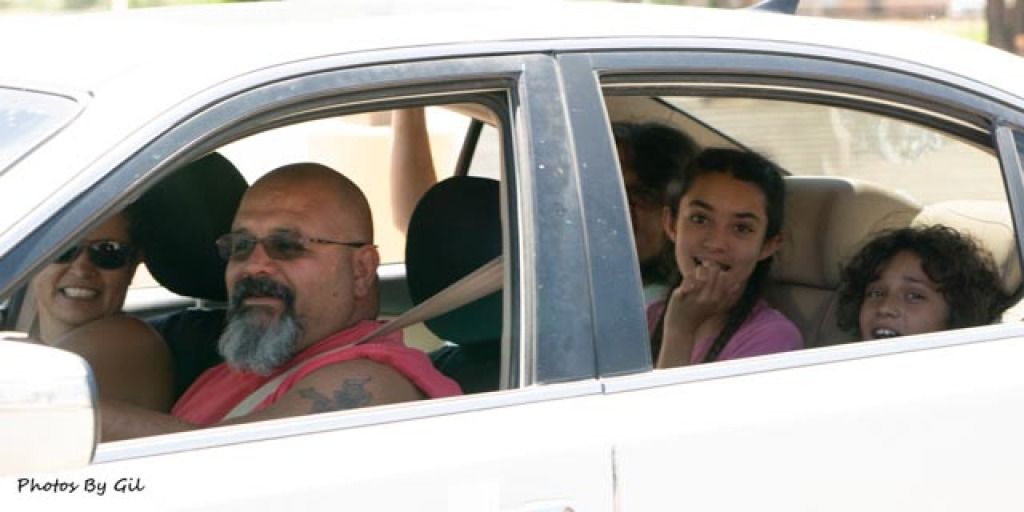 A family of four smiles inside a white car. 