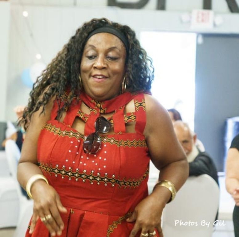 A woman in a red patterned dress smiles while dancing at an indoor event. 