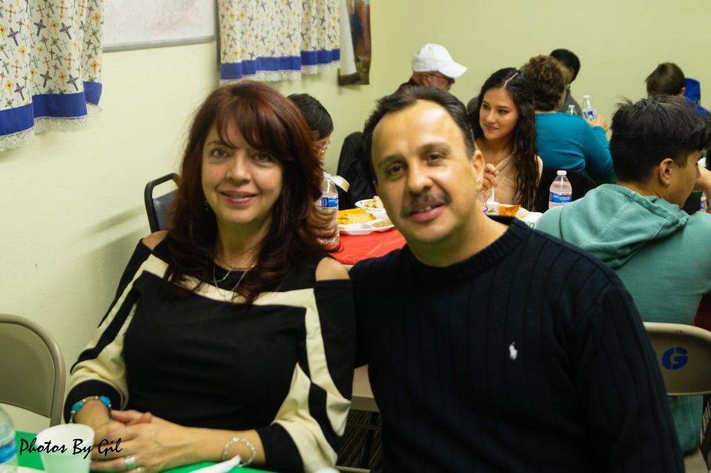 A smiling couple sits at a table in a lively gathering.