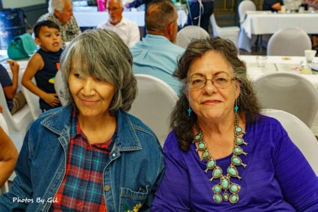 Two women sit together at a gathering, smiling warmly. 