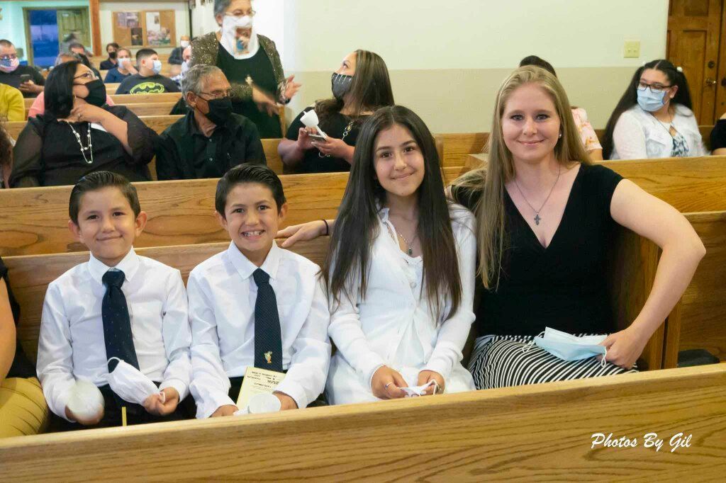 A group of four people in a church pew, three children and one adult woman, smiling. 