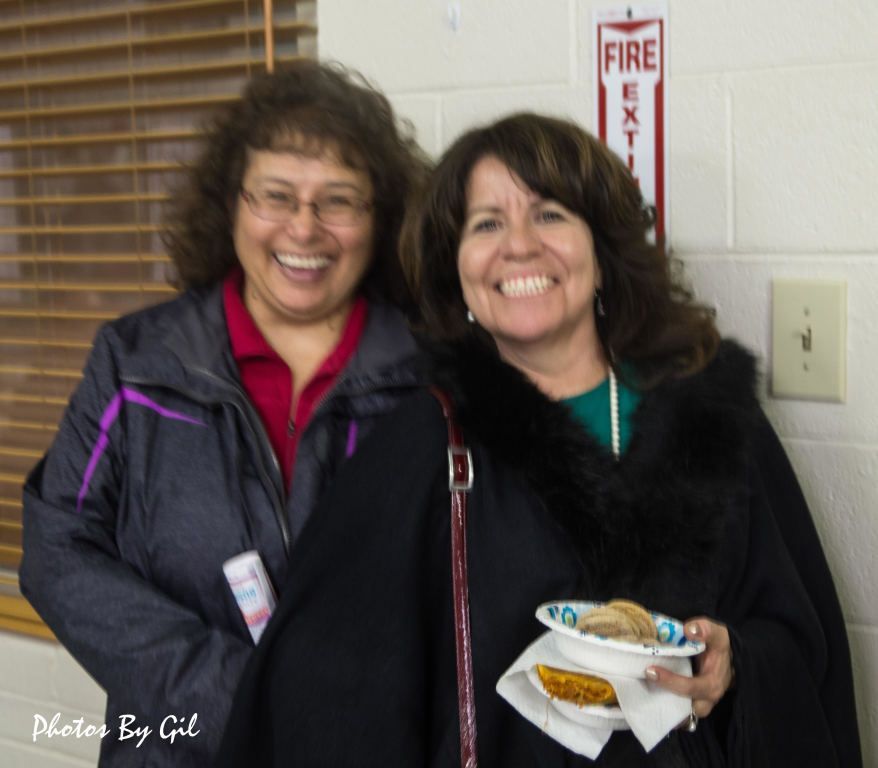Two women smiling warmly, standing indoors.