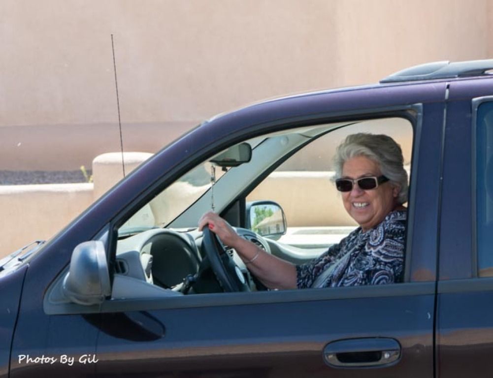 Smiling woman with gray hair and sunglasses driving a dark-colored SUV. 