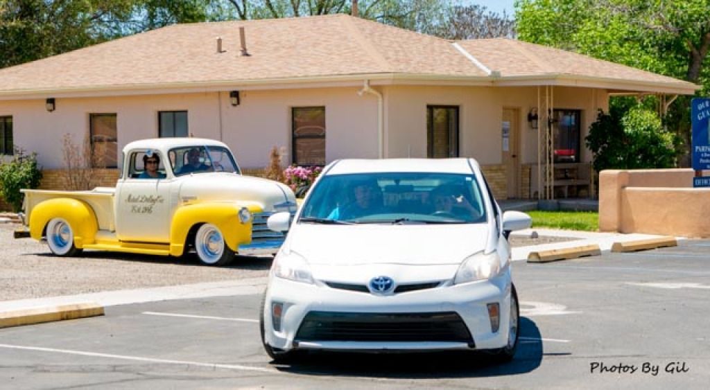 A white Toyota and a vintage yellow pickup truck are parked in front of a beige building.