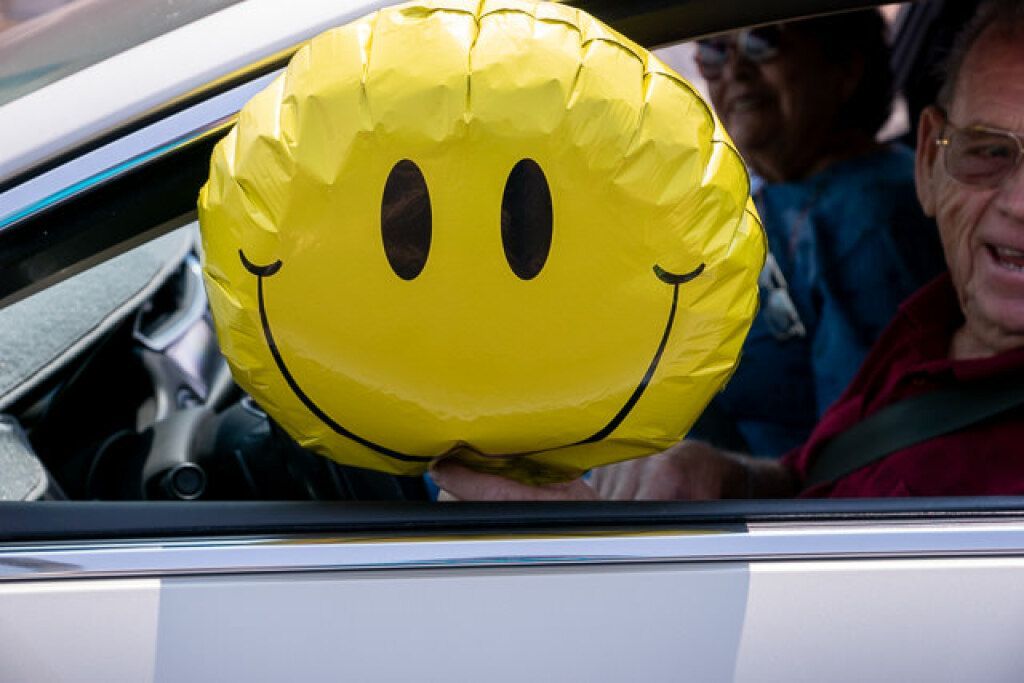 A person in a car holds a large yellow smiley face balloon.