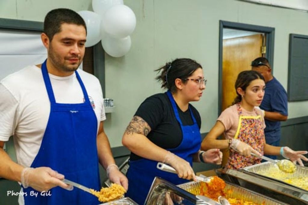 Three people serve food at a community event. 