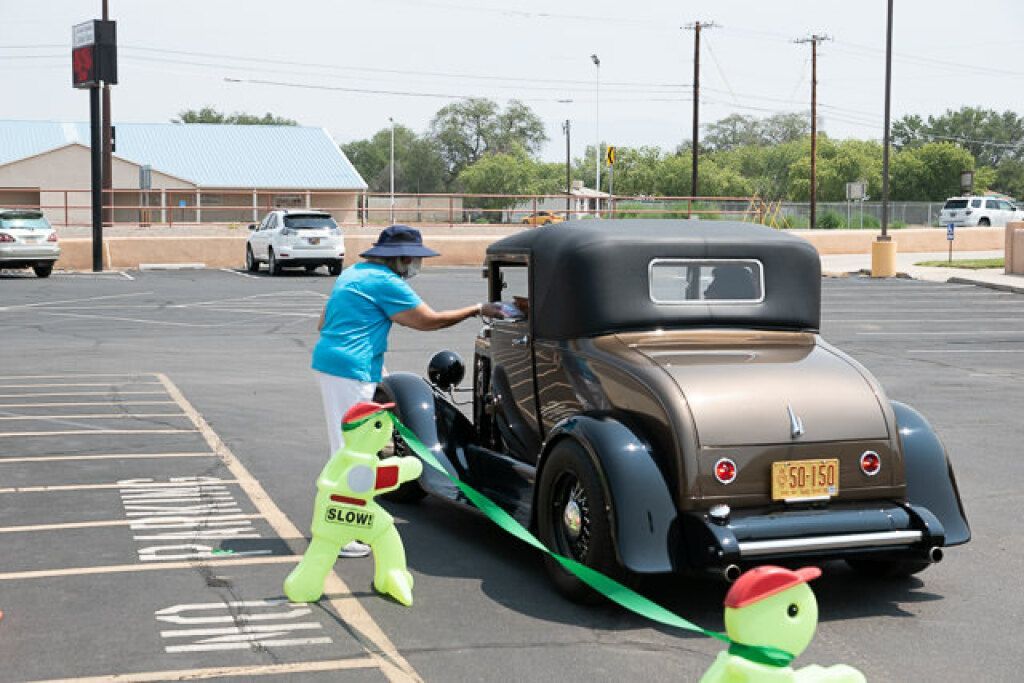A person in a blue shirt and hat leans into a vintage brown car in a parking lot. 