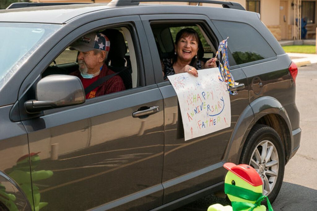 A woman joyfully leans out of a parked car.