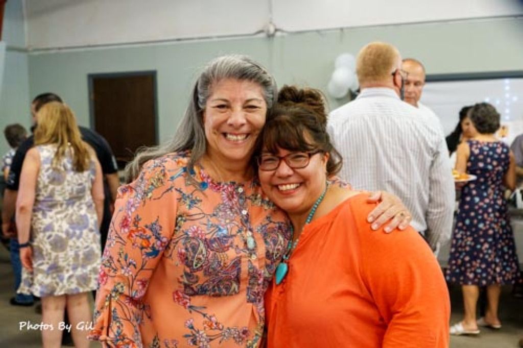 Two smiling women pose closely at an indoor event.