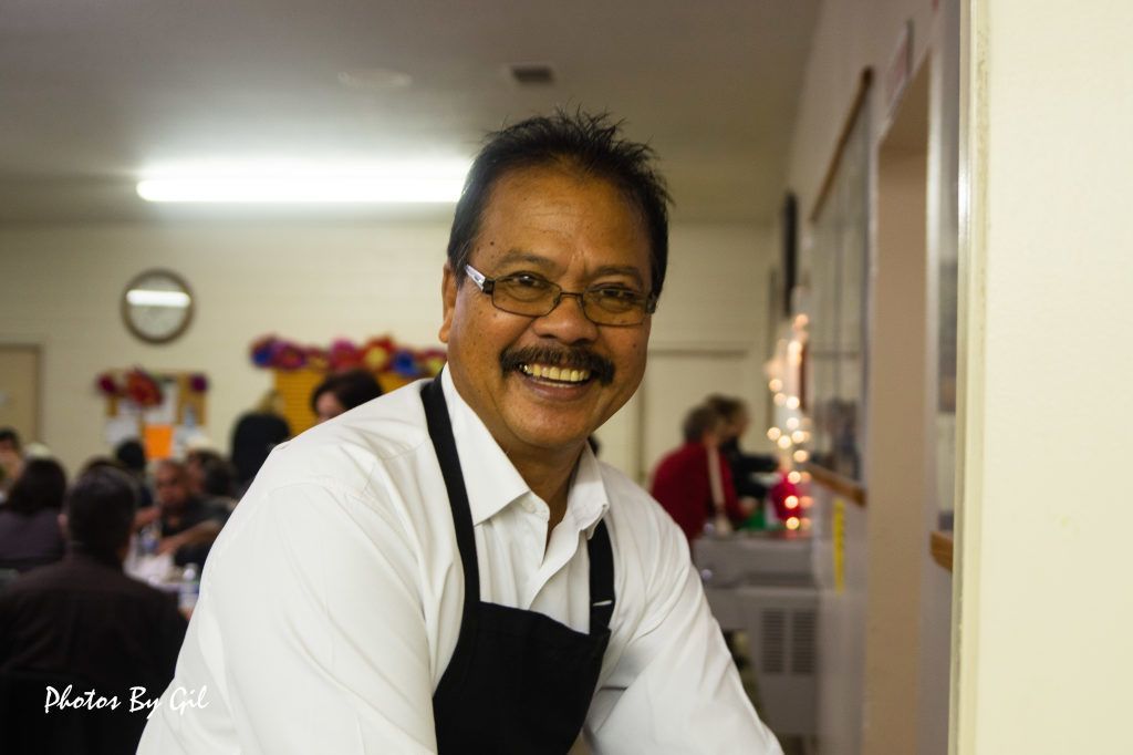 Smiling man with glasses and a mustache, wearing a white shirt and black apron.