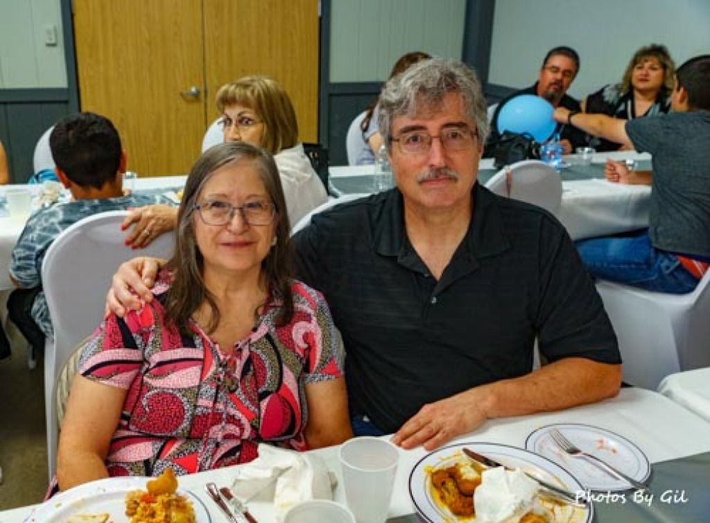 A smiling couple sits closely at a dining table filled with plates and cups.