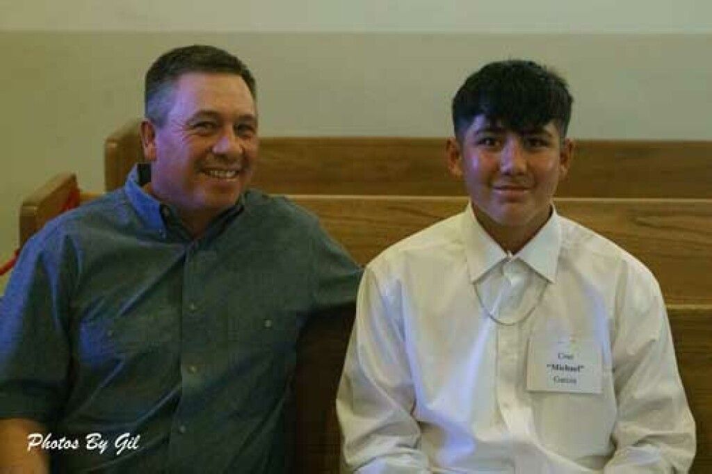 Two people sit on wooden pews, smiling warmly. 