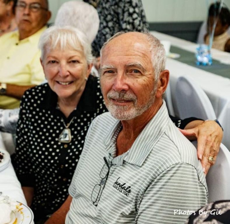 An elderly couple smiles warmly at a gathering. 