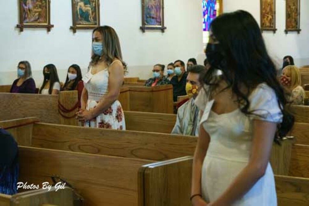 People in masks sit and stand in church pews, maintaining distance. 