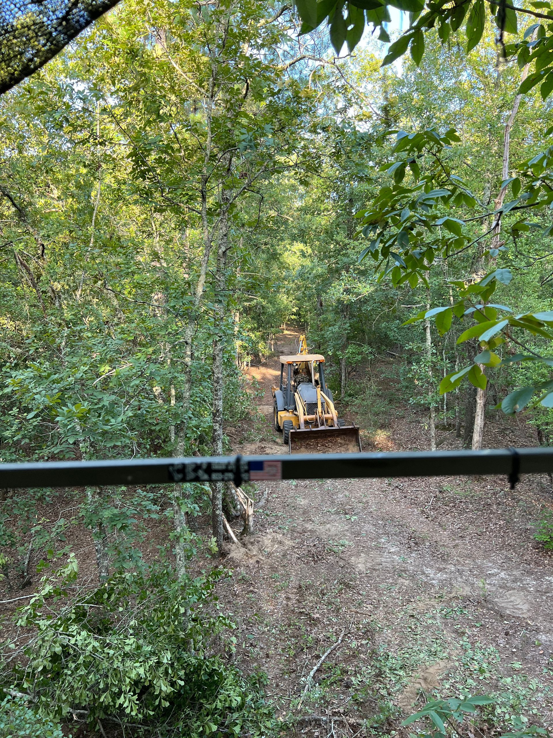 A bulldozer is driving down a dirt road in the woods.