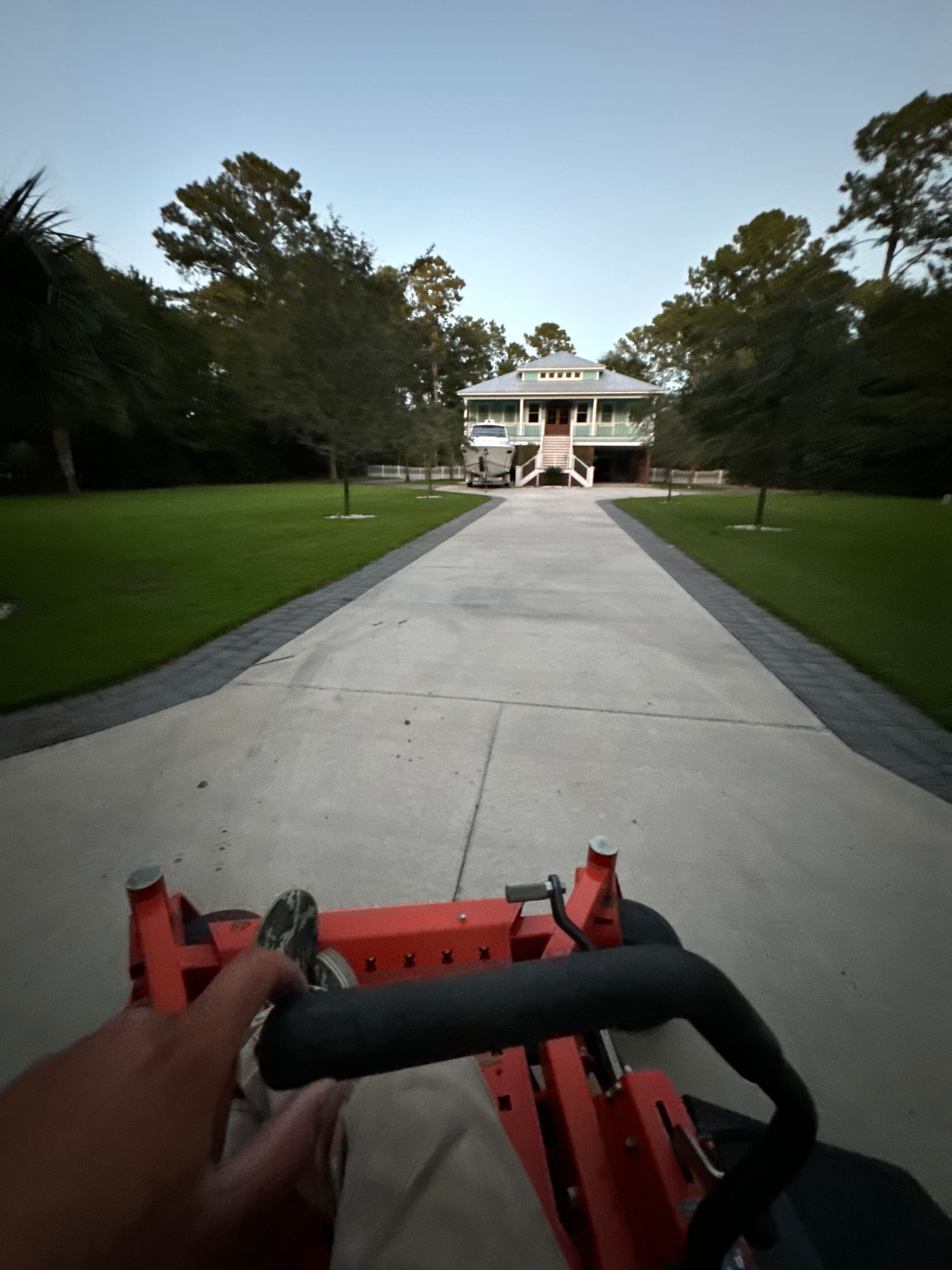A person is driving a lawn mower down a driveway towards a house