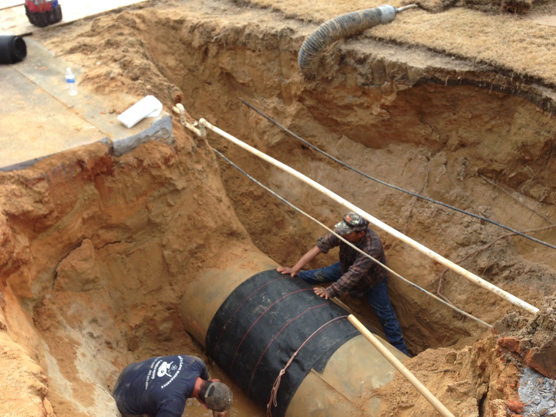 Two men are working on a large pipe in the dirt.