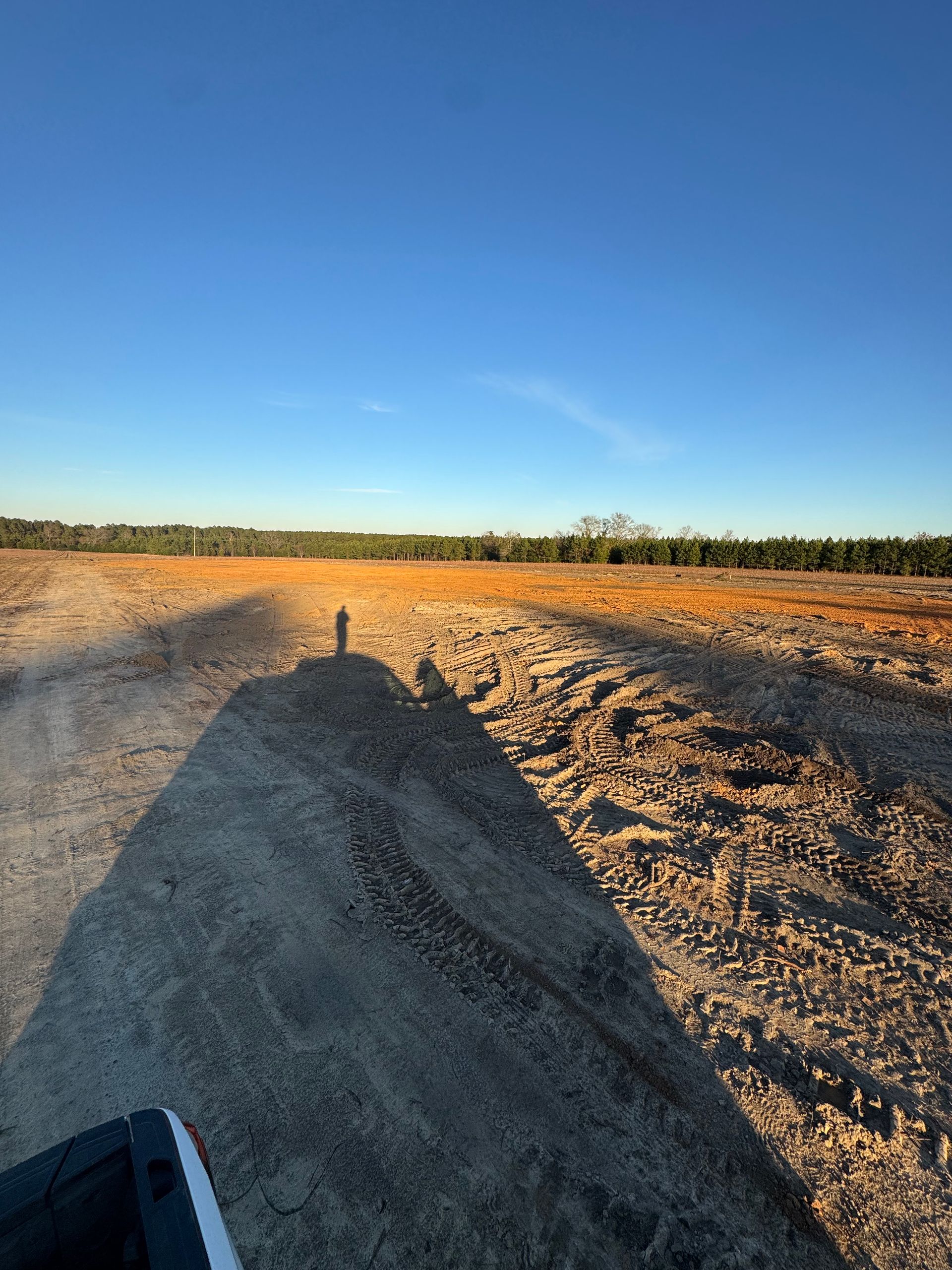 A shadow of a person is cast on a dirt road.