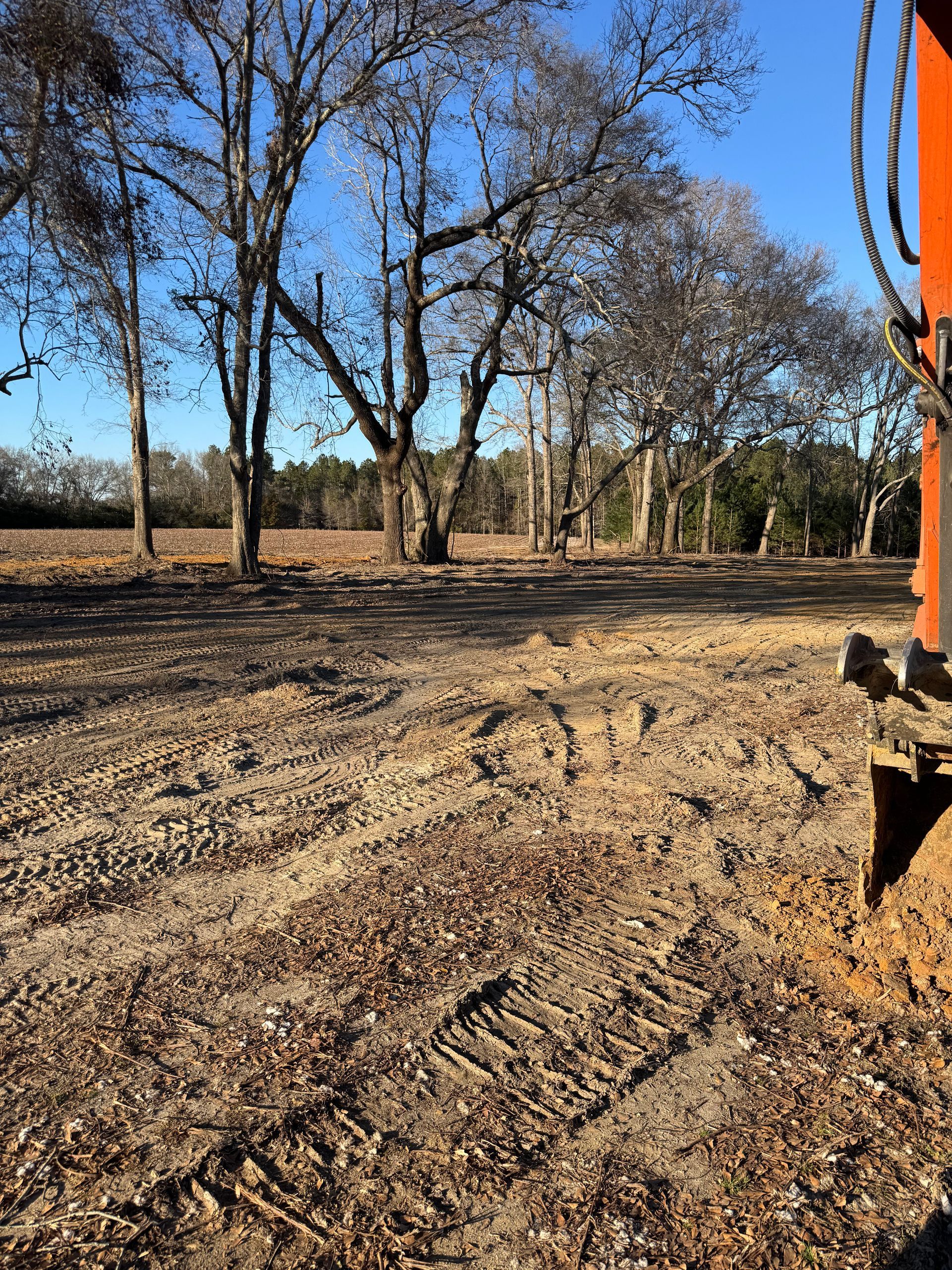A tractor is driving through a dirt field with trees in the background.