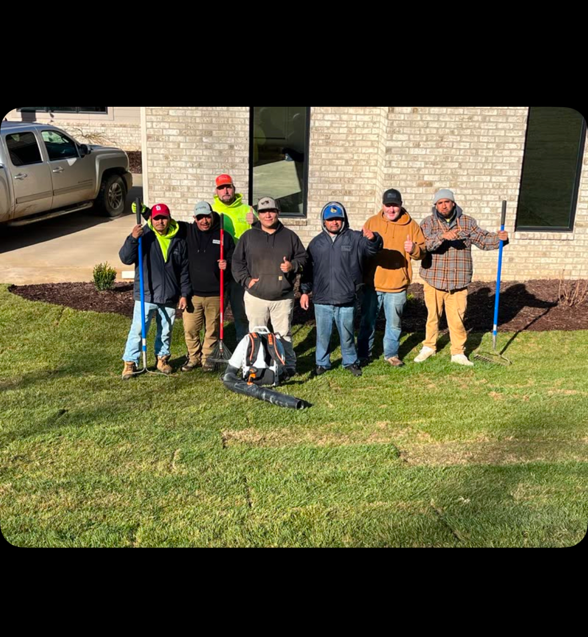 A group of men are standing in front of a house holding rakes.
