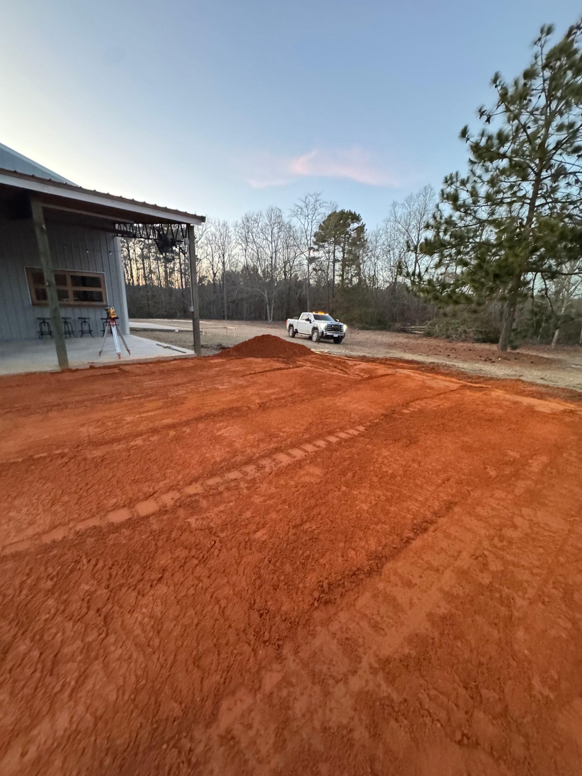A white truck is driving down a dirt road in front of a house.
