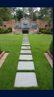 A lawn with a stone walkway leading to a fountain