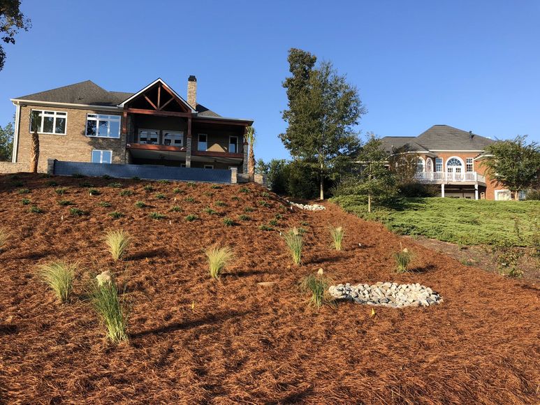 A large house is sitting on top of a hill surrounded by trees and mulch.